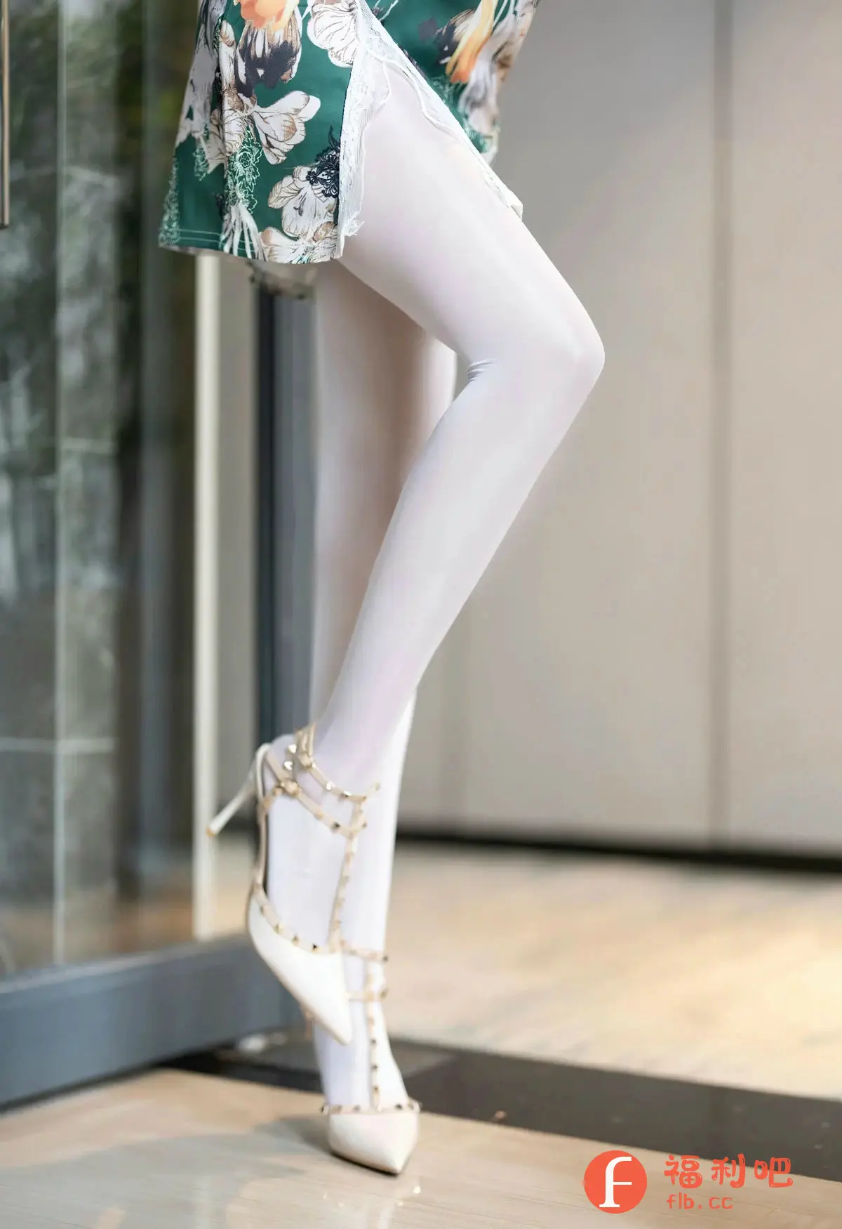 这张美女私房写真展现了她修长白皙的美腿，穿着紧身白色裤袜，完美勾勒出腿部线条，显得性感迷人。脚上搭配一双白色高跟鞋，鞋面设计独特，增添了时尚感。美女身穿一件印花短裙，裙边的白色蕾丝细节更显精致。整体造型简约而不失优雅，凸显了美女的姣好身材和迷人气质。背景干净整洁，更突出了人物主体，营造出一种私密而诱人的氛围。这组照片充分展现了女性的柔美和性感，让人赏心悦目。