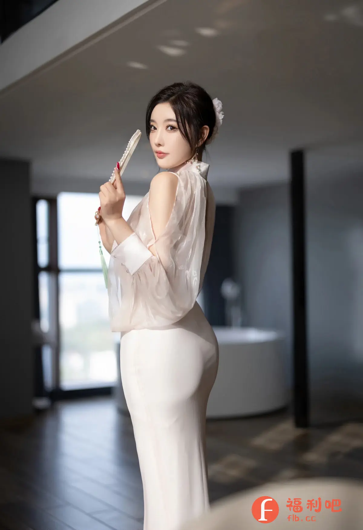 描述：这是一张优雅美女的室内写真。她身穿一套白色礼服，上身是轻盈的薄纱设计，露出香肩，下身是修身的包臀裙，完美勾勒出她的身材曲线。她手持一把带有珍珠装饰的扇子，增添了一丝古典韵味。她的头发盘起，一朵白色小花点缀在发间，衬托出她精致的五官和温柔的气质。背景是现代风格的室内装修，简约而富有质感，与她的优雅气质相得益彰。整体画面光线柔和，营造出一种温馨浪漫的氛围。她的眼神充满自信和魅力，让人不禁为之倾倒。