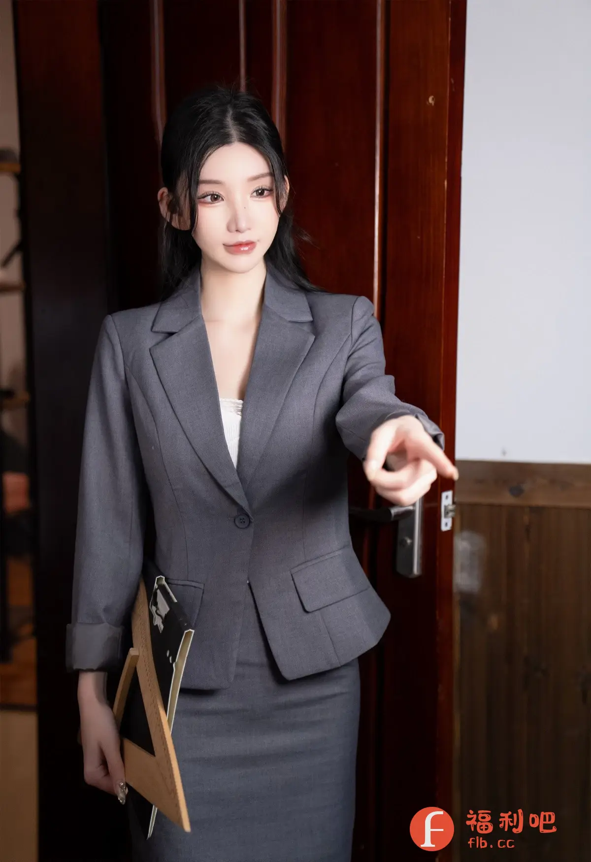 描述:照片中是一位身穿灰色职业套装的美女,她站在一扇棕色的木门前,看起来像是一位职场女性。她的头发乌黑亮丽,垂在肩头,精致的妆容突显出她清秀的五官。她身穿一件合身的灰色西装外套,内搭一件白色蕾丝内衣,下身搭配一条同色系的及膝裙,整体造型干练而优雅。
她手里拿着一个黑色的文件夹,另一只手伸出食指,指向画面之外,仿佛在指示方向或提出要求。她的表情严肃而认真,展现出她专业的一面。背景的木门和若隐若现的室内环境,为照片增添了一丝神秘感,也更显私房写真的独特魅力。整体色调偏暖,柔和的光线突显了她的肌肤质感,营造出一种舒适的氛围。