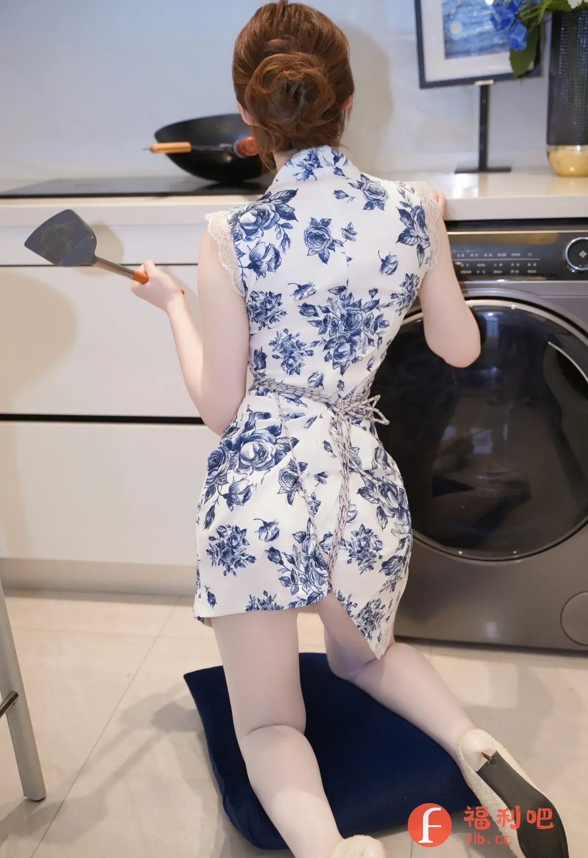 描述:照片中,一位背对着镜头的年轻女子跪坐在蓝色的垫子上,穿着一件白色底色、蓝色花朵图案的旗袍式连衣裙。她的头发盘成一个发髻,露出颈部和背部的线条。裙子的设计别致,带有蕾丝边,腰部用绳子束紧。她一只手拿着锅铲,似乎正在厨房忙碌。背景是现代化的厨房,有白色的橱柜和一台洗衣机。整体光线柔和,营造出一种温馨而私密的氛围。这可能是一组展示女性居家生活和时尚品味的私房写真。