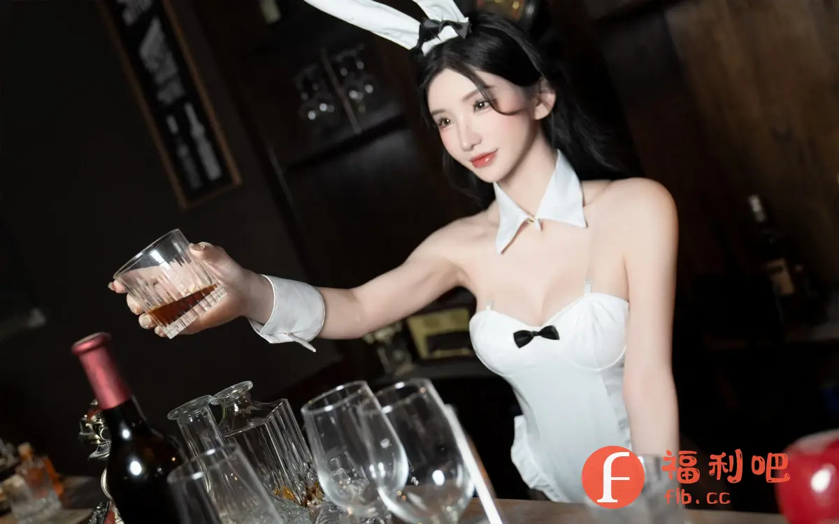 描述:图中是一位穿着白色兔女郎服装的年轻女性,她站在酒吧吧台后,手里端着一杯琥珀色的液体。她的服装包括一对兔耳朵、一个黑色领结和配套的袖套。她有着精致的妆容,黑色的长发垂肩。吧台上摆放着各种玻璃杯和酒瓶,包括一个红酒瓶。背景较为昏暗,整体场景充满了一种神秘和性感的气息。这应该是一张私房写真,突出女性的魅力和酒吧的氛围。