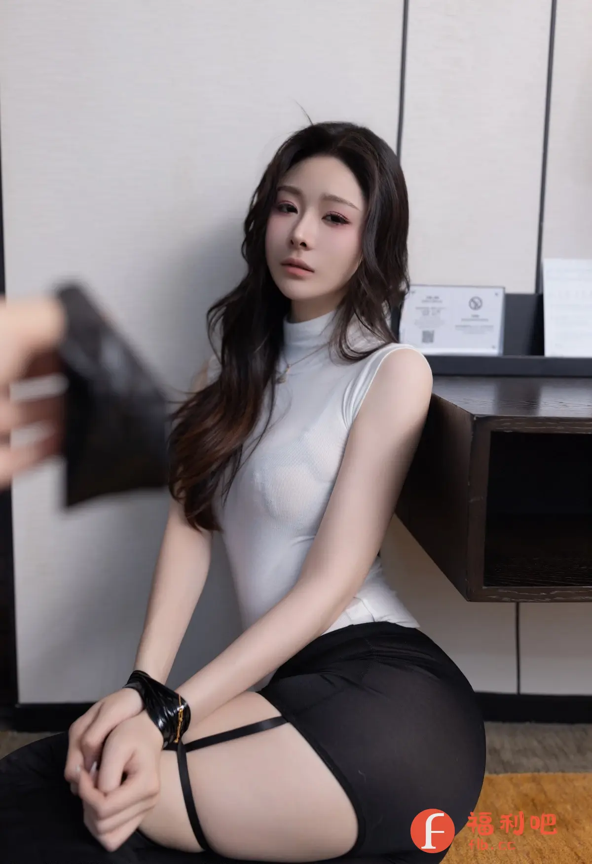 照片中的美女身穿白色无袖上衣和黑色短裙,坐在地上,展现出一种性感而优雅的气质。她的妆容精致,长发披肩,眼神深邃,吸引着人们的目光。裙子的设计独特,带有吊袜带的元素,增添了一丝神秘感。美女的手腕上戴着黑色的饰品,更显时尚品味。背景是简约的室内环境,更突出了美女的美丽。这张照片充满了诱惑力,同时又展现了女性的自信和魅力。