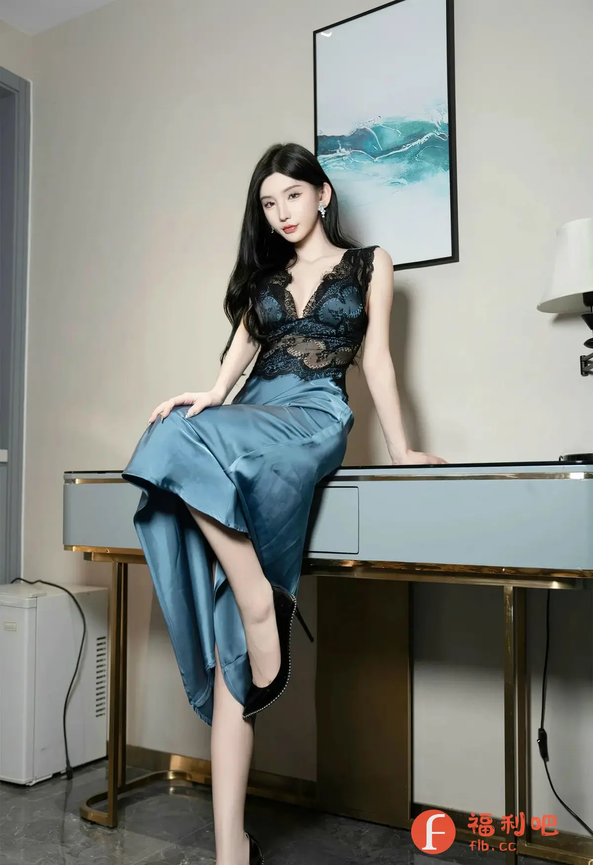 这张照片展现了一位优雅迷人的年轻女性。她身穿一件丝绸质地的蓝色吊带裙，裙子的上半部分是精致的黑色蕾丝设计，增添了几分性感与神秘感。她坐在一个浅灰色的梳妆台上，一双黑色高跟鞋突显了她的修长美腿。背景墙上挂着一幅抽象画，画面的色彩与整体的色调相呼应，营造出一种宁静而富有艺术感的氛围。整体构图简洁而富有美感，凸显了女性的优雅气质和曼妙身姿，是一张极具吸引力的私房写真。