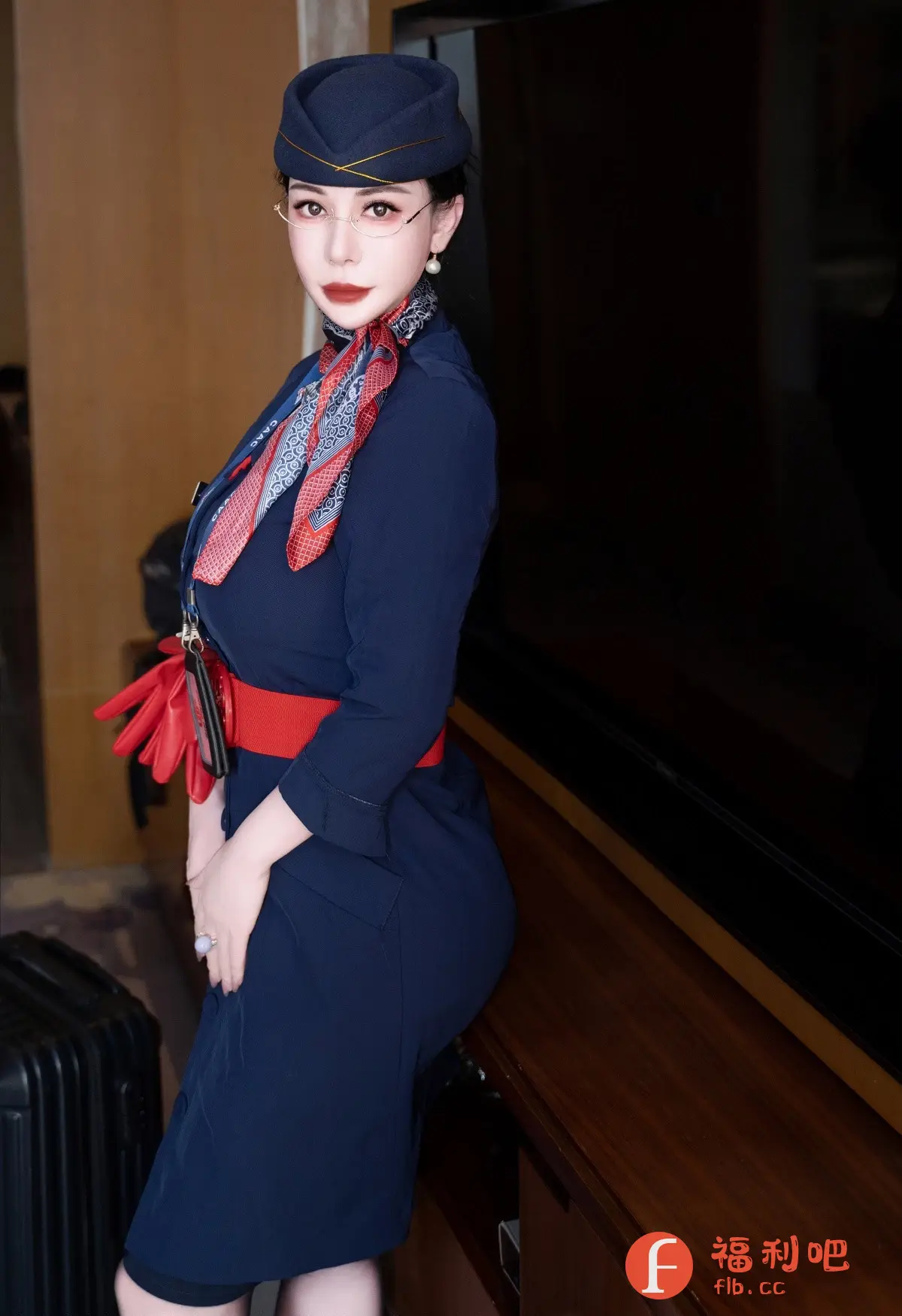 一位穿着空姐制服的美女倚靠在深色家具旁,展现出专业而优雅的形象。她头戴深蓝色空姐帽,佩戴着精致的眼镜和珍珠耳环,颈间系着一条印有图案的丝巾,更显气质。她的蓝色制服剪裁合身,腰间系着红色腰带,凸显出她的身材曲线。手中拿着一双红色手套,为整体造型增添了一抹亮色。照片背景简洁,深色的家具和行李箱暗示着旅途中的场景,可能是在酒店房间内拍摄。她的妆容精致,红唇和眼妆都恰到好处,展现出成熟女性的魅力。整体画面充满时尚感,既展现了空姐的职业形象,又突出了女性的个人魅力。
