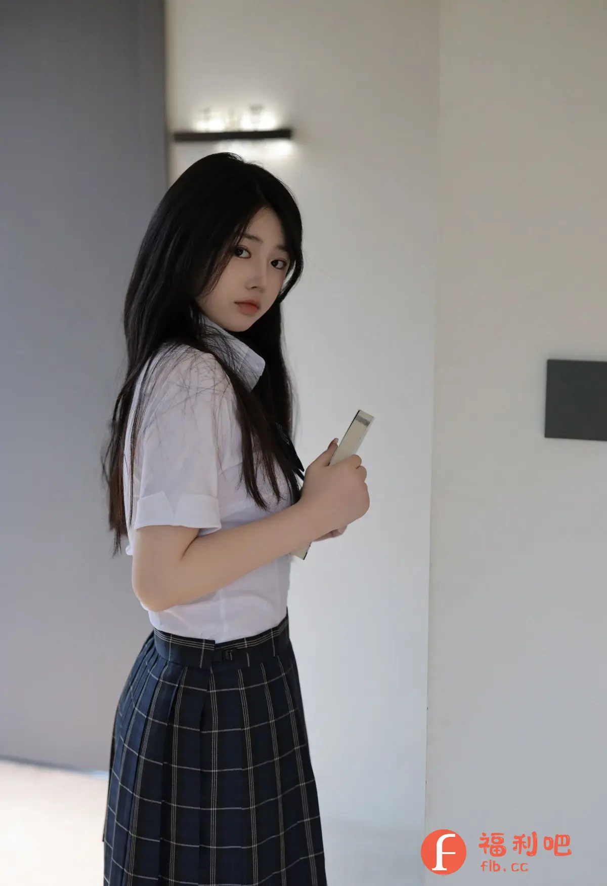 描述:照片中是一位年轻的亚洲女性,她穿着一套学生制服,包括一件短袖白色衬衫和一条格子裙。她的头发乌黑亮丽,自然地披在肩上。她手持着一个白色物体,可能是手机或书本。她的表情略带忧郁,眼睛直视镜头,给人一种清纯而又略带神秘的感觉。照片的背景简约,以浅灰色和白色为主,光线柔和,突出了人物的清新气质。整体风格偏向日系写真,充满了青春的气息。