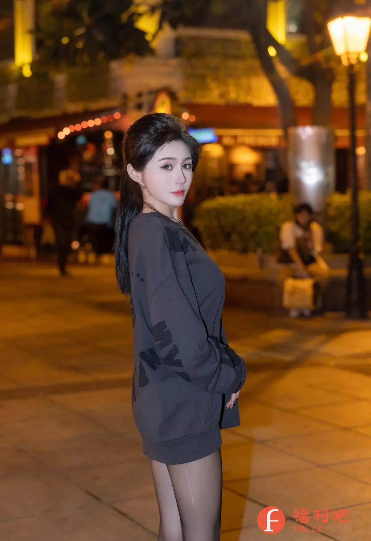 一位美丽优雅的亚洲女性在夜幕降临的街头摆姿势拍照。她穿着一件休闲的灰色长款卫衣,搭配着性感的黑色丝袜,更显腿部线条的修长。她的黑发梳成精致的发型,露出精致的五官,红唇动人,眼神温柔而充满魅力。背景是灯火辉煌的街道,树木和建筑物在灯光的映衬下显得格外迷人,营造出一种浪漫而神秘的氛围。整体画面充满了时尚感和艺术气息,让人不禁为她的美丽所倾倒。