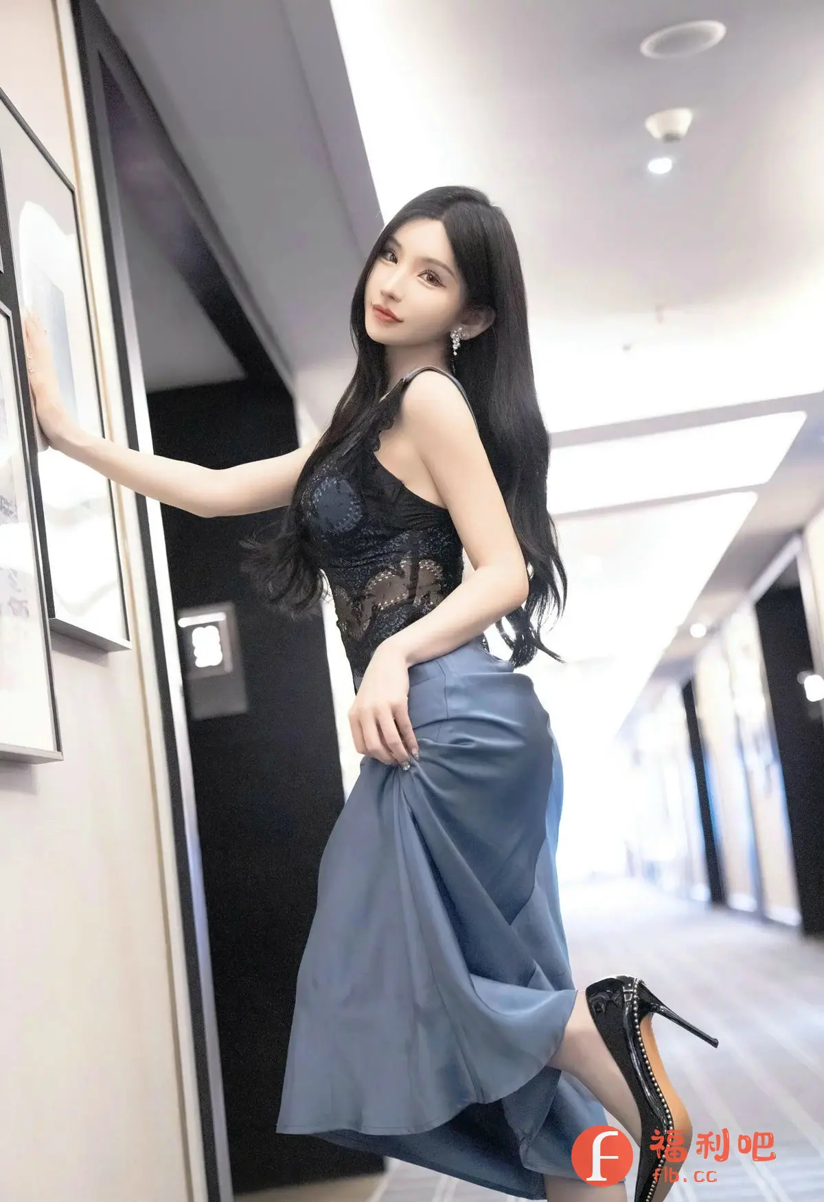 描述：照片中是一位身材姣好，容貌清丽的亚洲美女。她留着一头乌黑亮丽的长发，佩戴着精致的耳环。美女身穿一件带有蕾丝装饰的黑色吊带上衣，搭配一条丝滑的蓝色长裙，显得性感又优雅。她一只手扶在墙上的装饰画旁，另一只手轻轻提起裙摆，露出穿着黑色高跟鞋的纤细脚踝。美女微微侧身，眼神妩媚动人，充满自信。照片整体色调柔和，光线明亮，突显了美女的白皙皮肤和姣好身材。背景是现代风格的室内走廊，更增添了照片的时尚感。这是一张充满魅力和艺术感的私房写真。

返回格式：(描述：照片中是一位身材姣好，容貌清丽的亚洲美女。她留着一头乌黑亮丽的长发，佩戴着精致的耳环。美女身穿一件带有蕾丝装饰的黑色吊带上衣，搭配一条丝滑的蓝色长裙，显得性感又优雅。她一只手扶在墙上的装饰画旁，另一只手轻轻提起裙摆，露出穿着黑色高跟鞋的纤细脚踝。美女微微侧身，眼神妩媚动人，充满自信。照片整体色调柔和，光线明亮，突显了美女的白皙皮肤和姣好身材。背景是现代风格的室内走廊，更增添了照片的时尚感。这是一张充满魅力和艺术感的私房写真。)