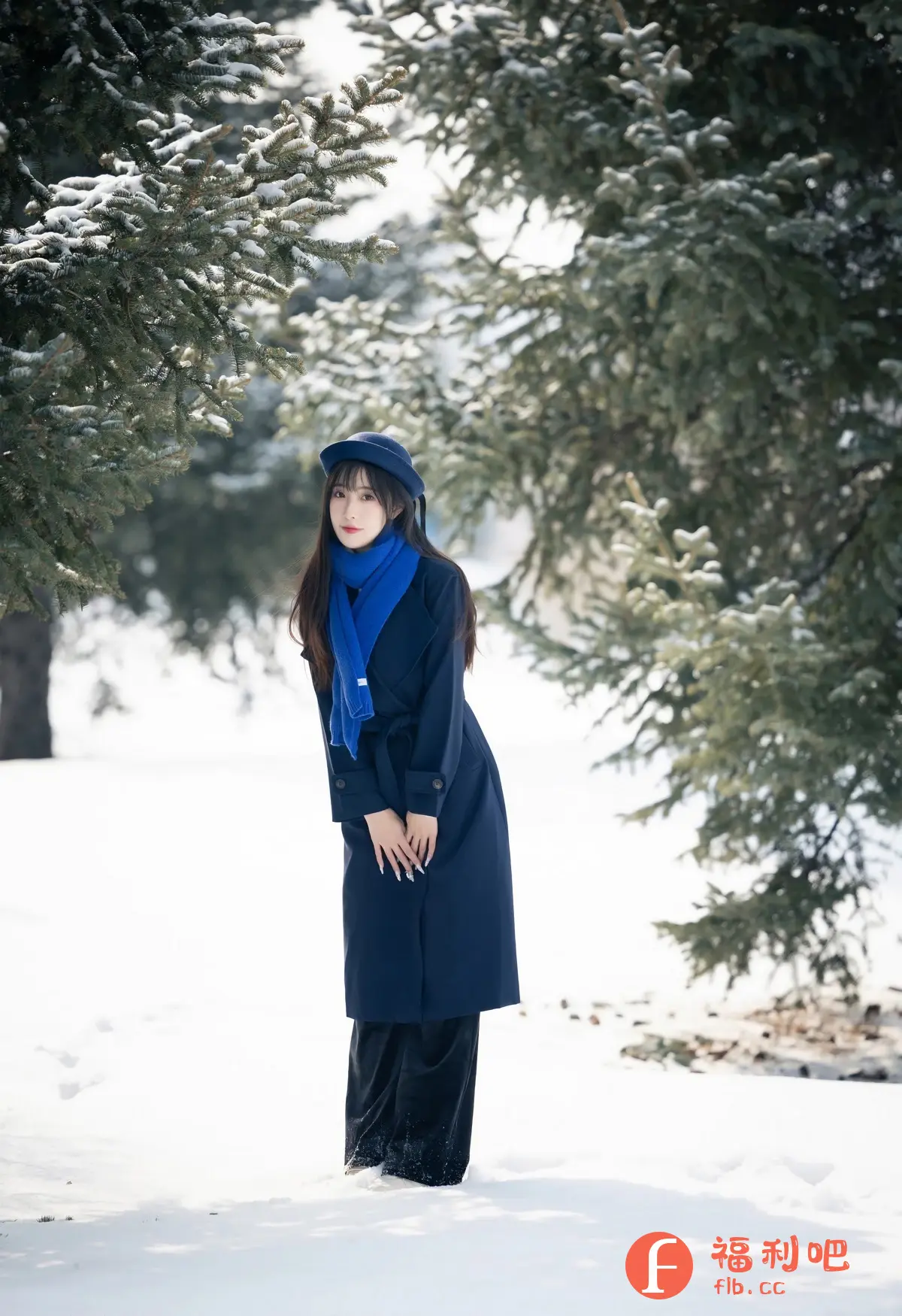 一位年轻美丽的亚洲女性站在雪地里,周围环绕着覆盖着积雪的绿色树木。她身穿一件深蓝色长款外套,搭配同色系的帽子和一条亮蓝色围巾,整体造型时尚而保暖。她长长的黑发垂在肩上,衬托出她精致的五官和白皙的皮肤。她双手交叠在身前,指甲修长,摆出略带羞涩的姿势,眼神温柔地看向镜头。背景是白茫茫的雪地和绿色的树木,营造出一种宁静而美丽的冬日氛围。整体画面清新自然,展现了女性的优雅气质和冬日的美好意境。