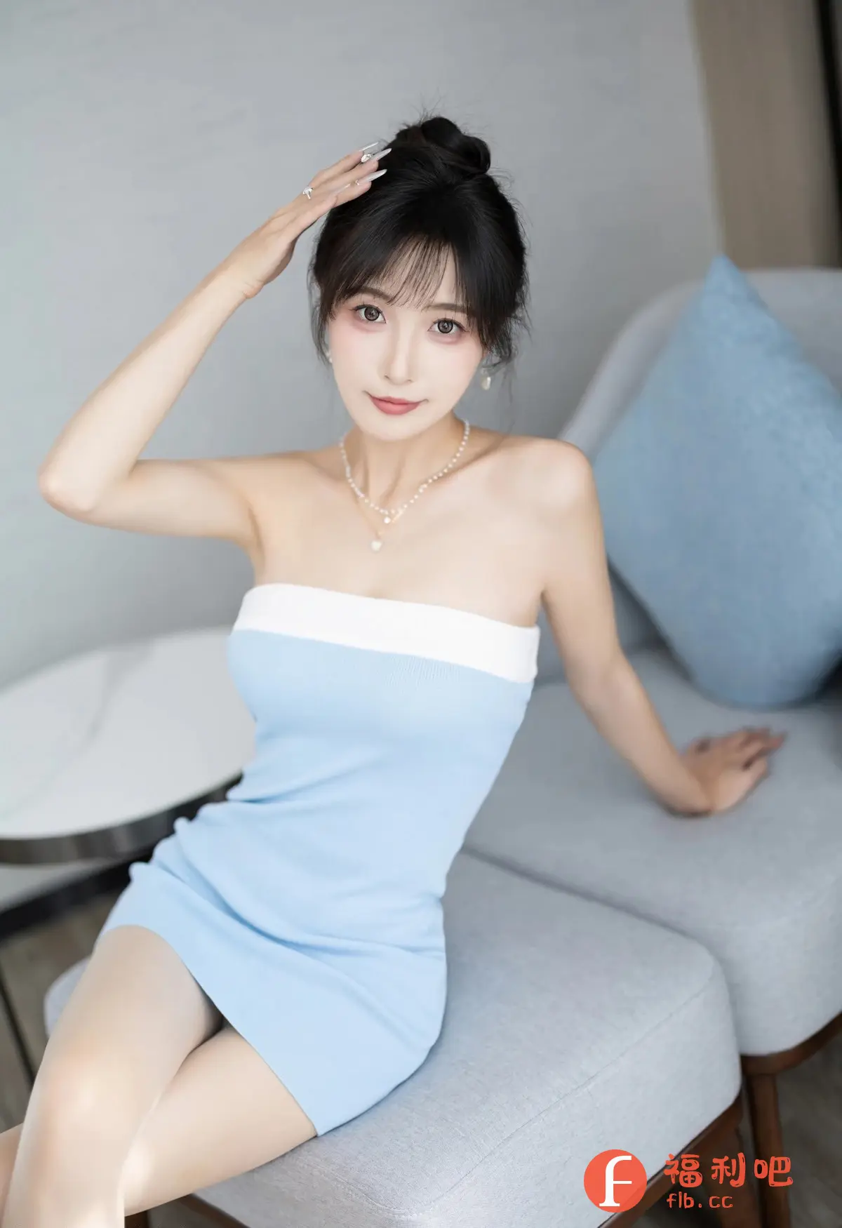 一位年轻女子坐在沙发上,身穿蓝色连衣裙,领口有白色点缀。她微微一笑,左手抬起轻抚头发,姿态优雅。女子的头发盘成发髻,露出精致的五官,妆容淡雅,凸显其清新自然的气质。她佩戴着珍珠项链和耳环,更添一丝高贵。沙发和背景色调柔和,营造出一种温馨舒适的氛围。整个画面色彩和谐,人物形象鲜明,给人以美的享受。