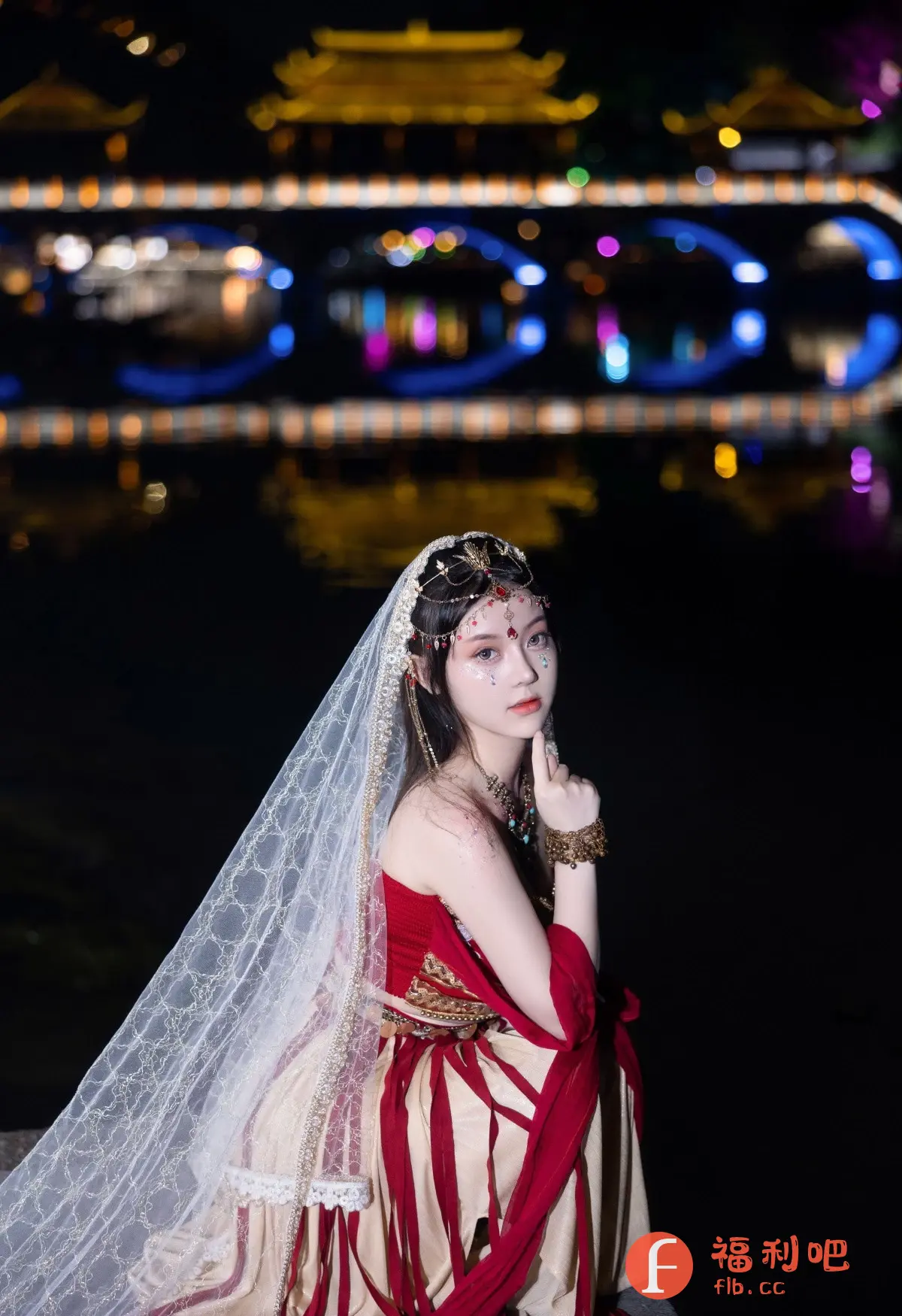 这张照片是一位身着华丽服饰的年轻女性的私房写真。她身穿红色和金色相间的传统服装,头戴精致的头饰,面纱轻柔地垂下。她的妆容精致,眼角点缀着闪亮的装饰,更显妩媚动人。她用食指轻点嘴唇,似乎在思考着什么,眼神中充满了神秘感。
背景是一个夜景,远处的桥梁和建筑灯火辉煌,倒映在平静的水面上,营造出一种梦幻般的氛围。整个画面充满了东方风情,既展现了女性的柔美和优雅,又增添了一丝神秘和浪漫。