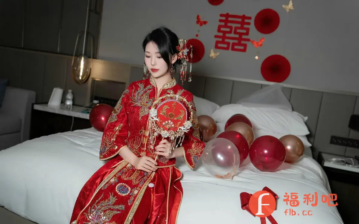 照片中,一位身穿红色传统中式礼服的年轻女性坐在床上,手持一柄精致的红色圆形扇子。她的头发盘起,佩戴着华丽的发饰,面容姣好,神情温婉。背景是布置过的房间,墙上贴着红色的喜字和圆纸片,还有一些蝴蝶装饰,床上散落着红色和金色的气球,以及一个红色的蝴蝶结。整体氛围温馨喜庆,充满着浓浓的中国传统婚礼气息。这可能是一张新娘在婚房中的私人写真,展现了她优雅美丽的一面。