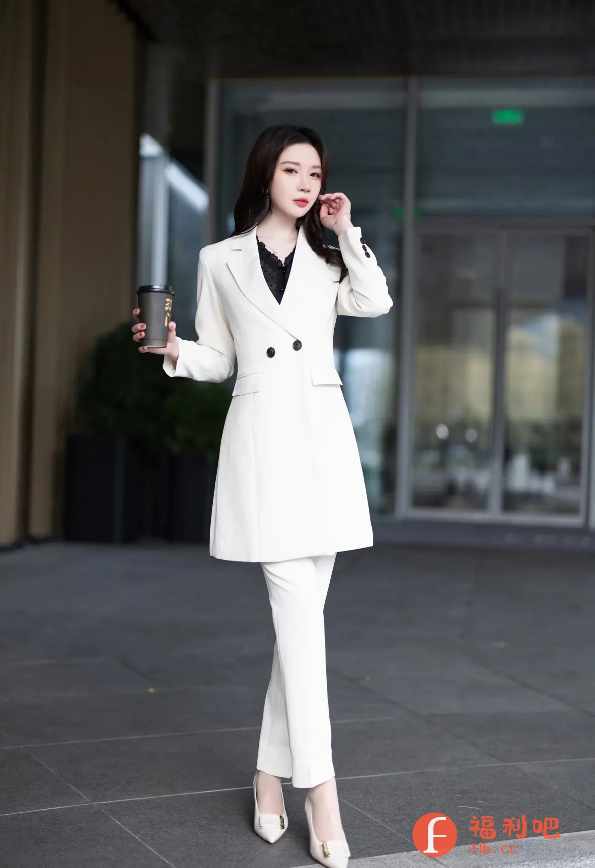 照片中一位身穿白色职业套装的亚洲美女,她手持咖啡杯,站在现代化的建筑前。套装剪裁得体,上衣类似长款西装,搭配同色系的修身长裤和白色高跟鞋,整体造型干练而优雅。她内搭一件黑色蕾丝上衣,增添了一丝性感和精致感。美女留着乌黑的长发,略带波浪,随意地披在肩上。她妆容精致,红唇鲜艳,眼神妩媚,手指轻抚头发,姿态优雅自信。背景是现代化的玻璃建筑,环境干净整洁,突显了她的时尚品味和职业形象。这应该是一张时尚写真或街拍,展现了现代都市女性的魅力。
