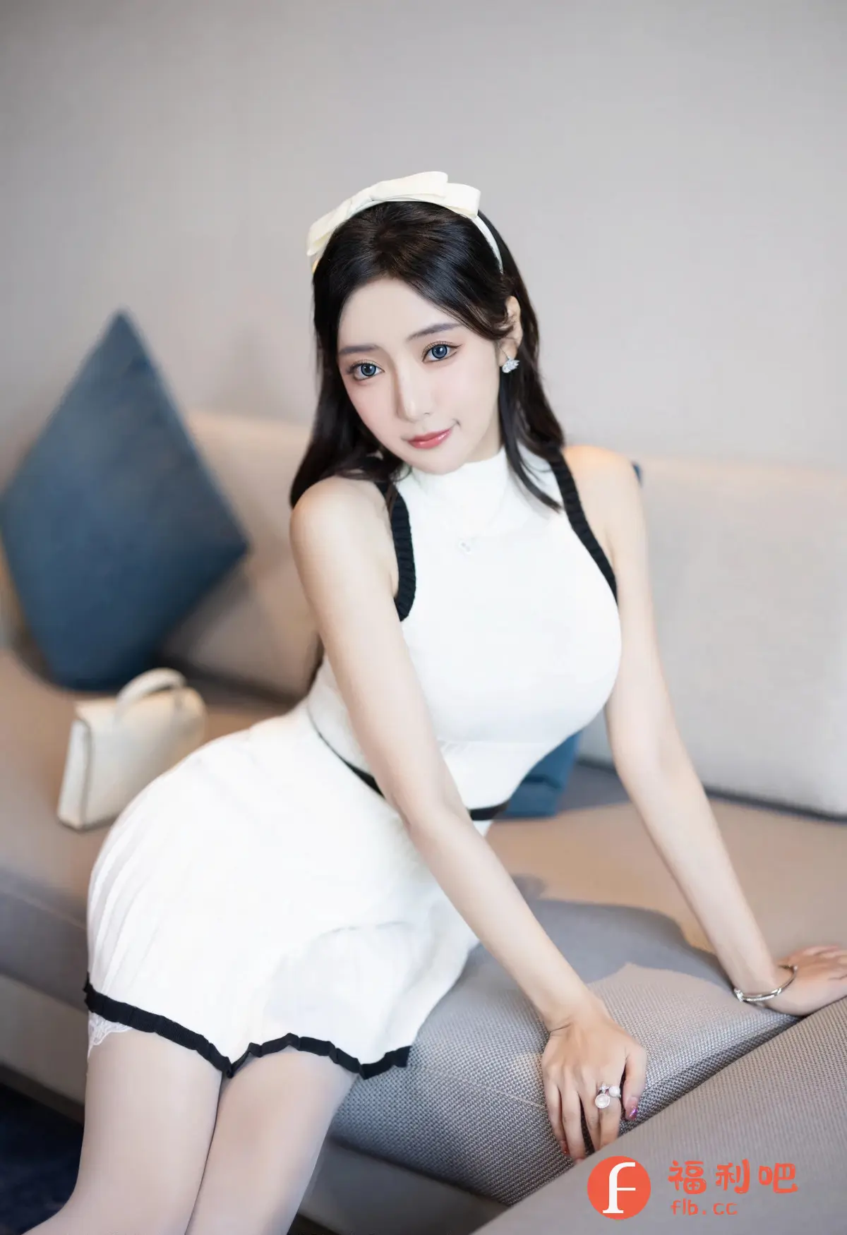 照片展示了一位年轻漂亮的亚洲女性的私房写真。她坐在一个灰色沙发上,姿势优雅而略带妩媚,表情柔和。她身穿一件白色连衣裙,连衣裙采用黑边设计,简洁时尚,更显其青春活力。她还佩戴了一个白色发箍,使得整个造型更加甜美可爱。镜头聚焦于她的上半身,展现了她精致的五官和白皙的皮肤。房间背景简约现代,浅色的墙壁和沙发营造出一种温馨舒适的氛围。沙发上摆放着一个蓝色靠枕和一个白色手提包,增添了画面的层次感和细节。整体来说,照片的构图和光线都处理得很好,突出了人物的美丽和气质,营造出一种轻松愉悦的氛围。