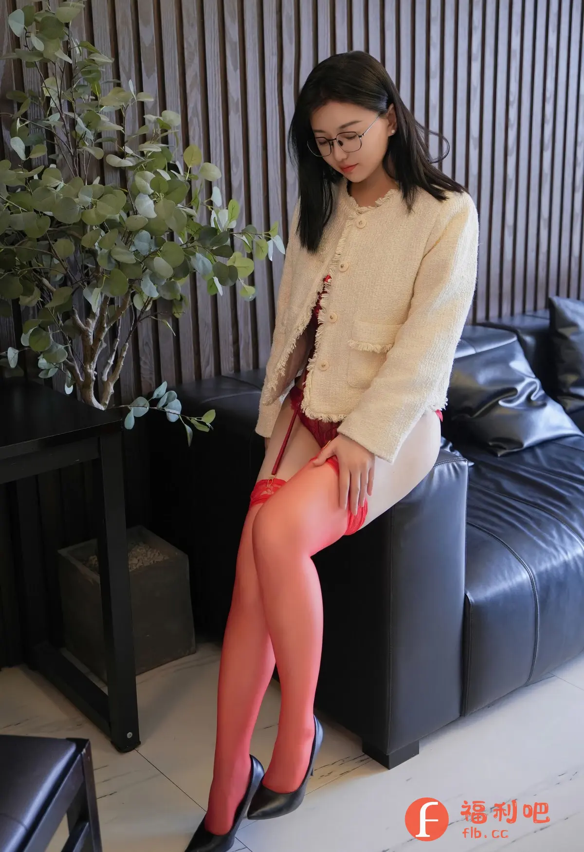 照片中,一位亚洲女性身穿米白色粗花呢外套,内搭红色蕾丝内衣,下身穿着红色吊袜带和黑色高跟鞋,性感迷人。她戴着眼镜,黑发柔顺地披在肩上,低头凝视着自己的腿部。她坐在一个黑色皮质沙发上,沙发旁边摆放着一个黑色小桌子,桌子上摆放着一盆绿植,为画面增添了一丝生机。背景是深色的木质墙面,营造出一种简约而时尚的氛围。整个画面充满了诱惑和艺术感。