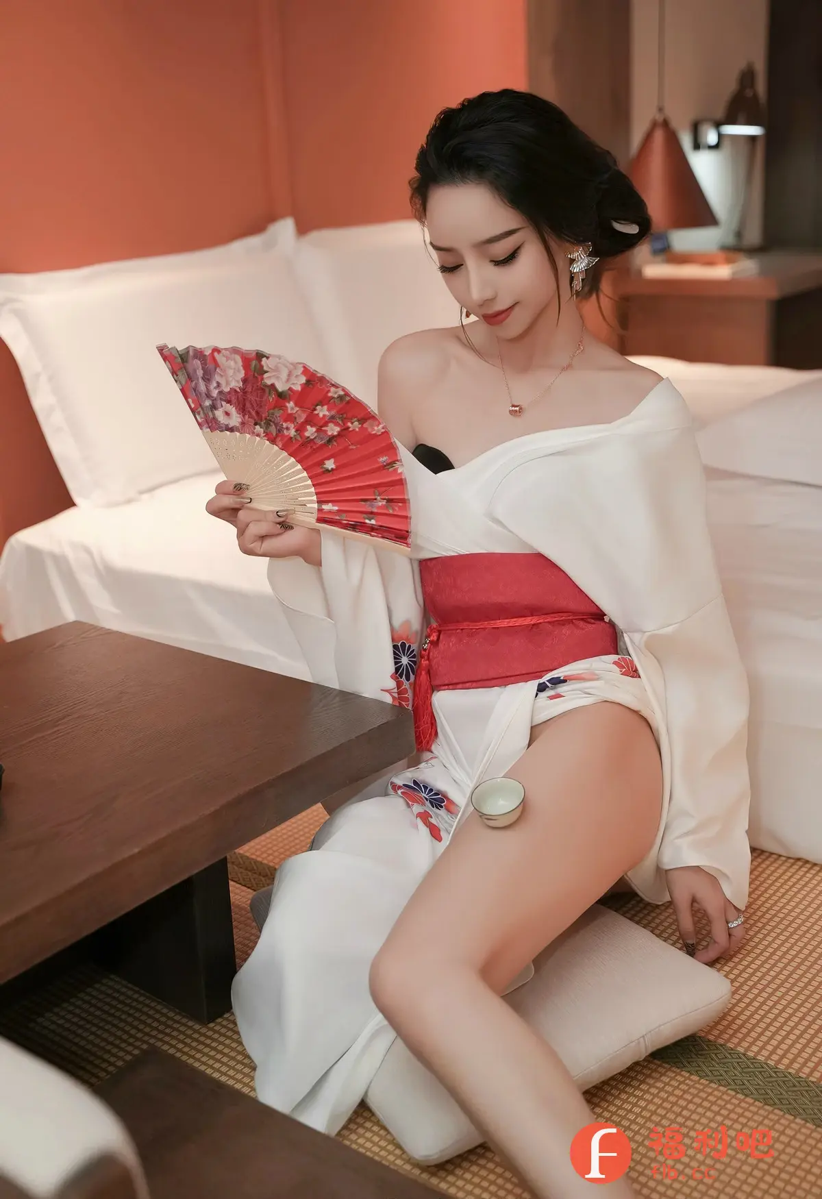 照片中,一位身材姣好的年轻女子身着白色和服,搭配红色腰带,坐在榻榻米上。她手持一把绘有花朵图案的红色折扇,神情专注地注视着扇面。她的发型精致,配有闪亮的首饰。一只小茶杯稳稳地放在她的大腿上,展示出她高超的平衡能力。背景是舒适的卧室环境,白色床铺和暖色调的墙壁营造出温馨的氛围。整体画面散发出一种优雅、性感而神秘的气息,仿佛一位古典美女正在享受她的私人时光。