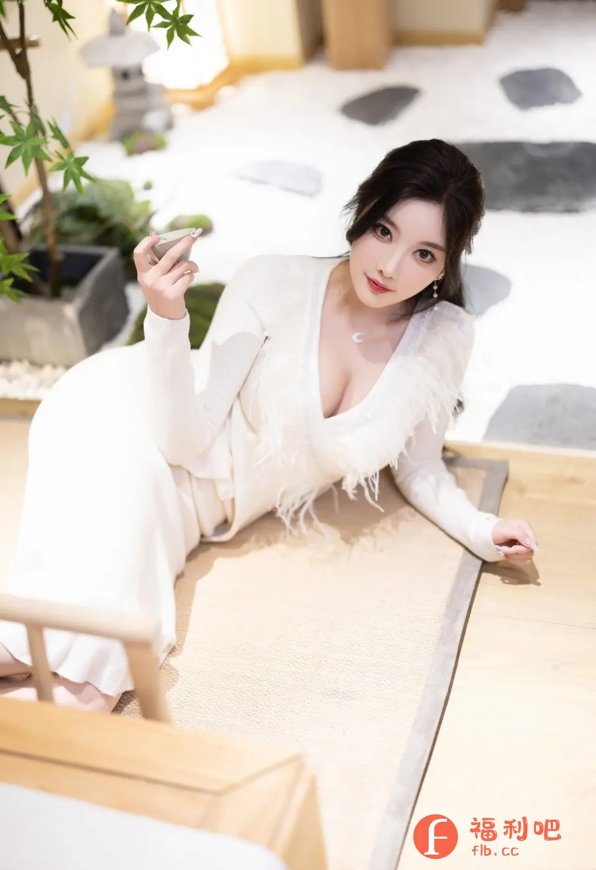 这张照片是一位美丽的亚洲女性的私房写真。她穿着一身优雅的白色连衣裙,连衣裙的领口设计独特,饰有白色羽毛,更显性感妩媚。她斜躺在地板上,一只手拿着一个小巧的容器,似乎在品味茶或酒。她的头发乌黑亮丽,妆容精致,眼神充满魅力。背景是一个日式风格的房间,摆放着盆栽和石灯笼,营造出一种宁静而富有艺术气息的氛围。整体画面光线柔和,色彩清新,突出了女性的柔美和优雅。