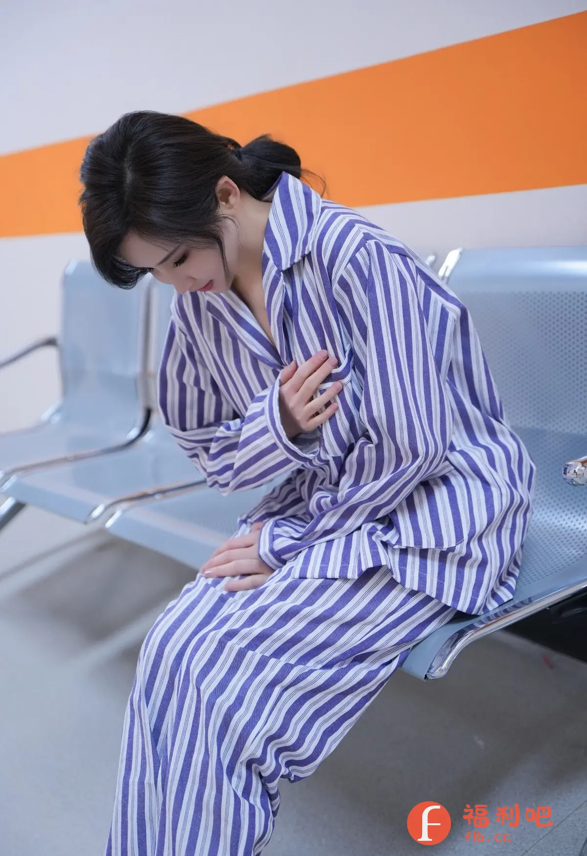 照片中,一位年轻女性身穿蓝白条纹病号服,神情落寞地坐在医院的蓝色等候椅上。她的头微微低下,眼神忧郁,一只手紧紧按在胸口,仿佛正在承受某种痛苦,另一只手则轻轻放在膝盖上。她的头发梳成一个简单的马尾,露出精致的侧脸,虽然憔悴,却依然显得美丽动人。背景是医院的墙壁,米白色和橙色相间,为整个画面增添了一丝冷清感。整张照片给人一种压抑和不安的感觉,让人不禁想知道她经历了什么,又在等待着什么。病号服的宽松感与她消瘦的身形形成对比,更突显出她的脆弱和无助。这是一张充满故事感的照片,能够引发观者内心深处的共鸣。