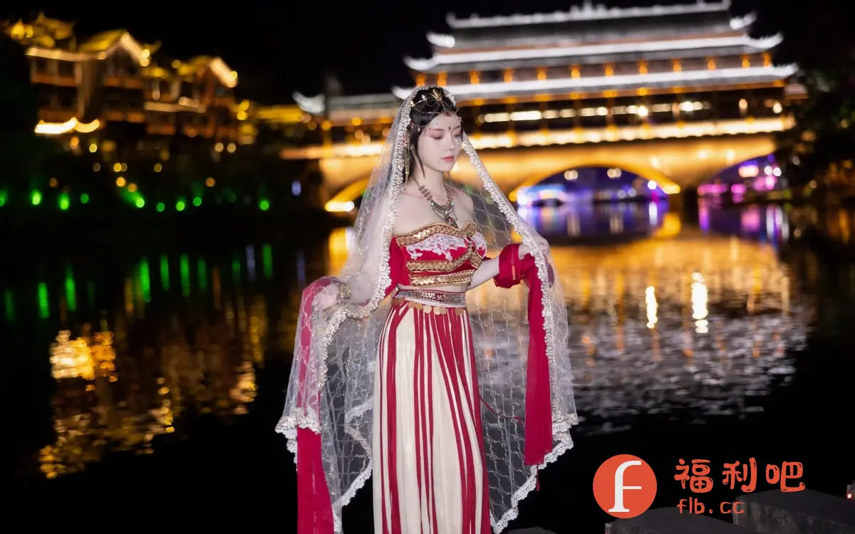 这张照片拍摄于夜晚,背景是灯光璀璨的古镇建筑和倒映在水中的光影,营造出一种梦幻般的氛围。照片的主角是一位身着传统服饰的年轻女性,她的服装华丽而精致,头饰和配饰都显得非常考究。她身披轻纱,手持红绸,姿态优雅,仿佛一位来自古代的仙女。她的眼神柔和,表情略带忧郁,更增添了几分神秘感和古典美。整张照片的光线处理得恰到好处,既突出了人物的美丽,又烘托了环境的氛围。照片整体风格唯美,古典,充满东方韵味。
