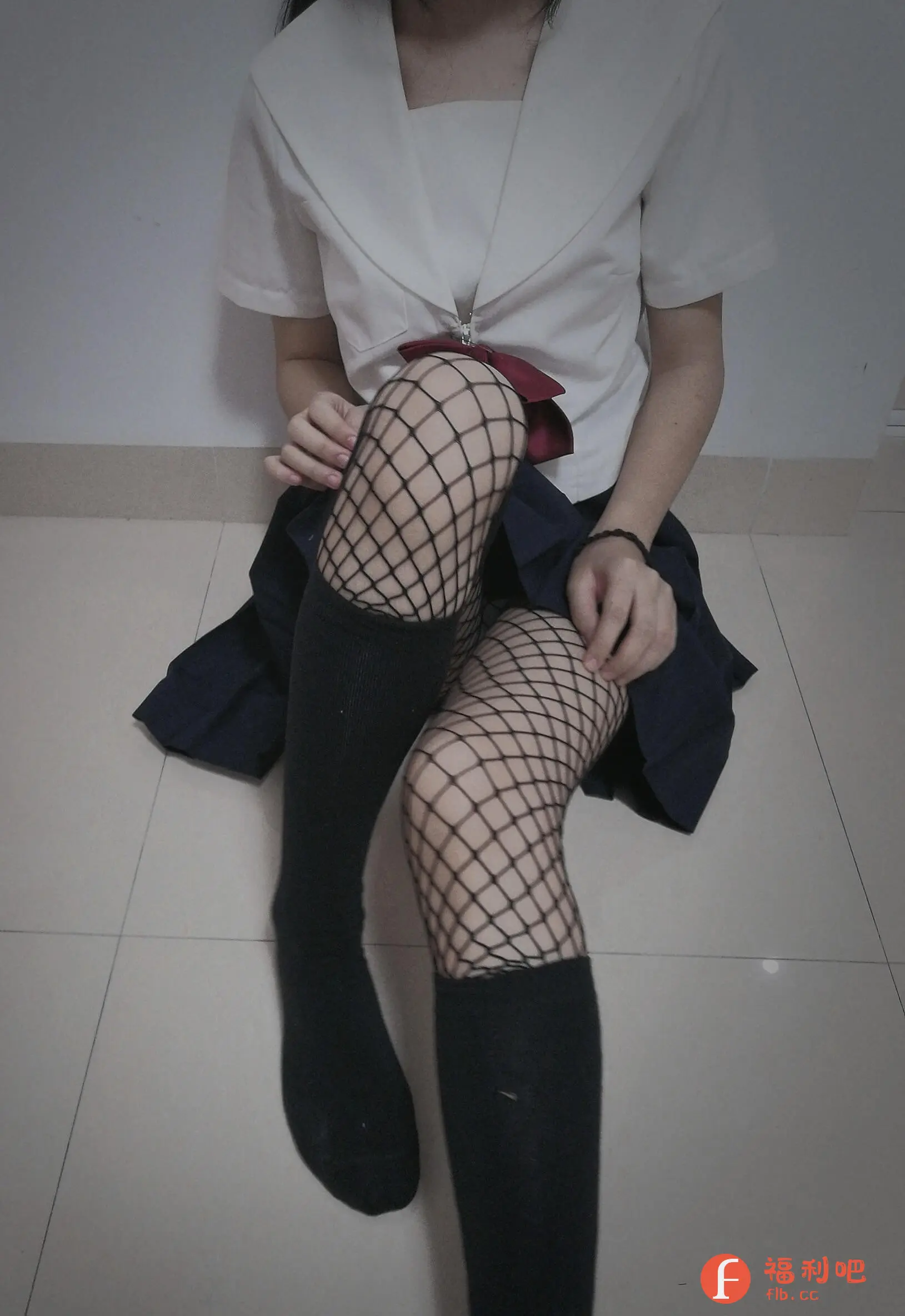 这张图片展示了一位女性穿着日系制服风格的服装,坐姿随意地靠墙而坐。她上身穿着一件白色水手服衬衫,领口系着一个红色的蝴蝶结,下身搭配一条深蓝色百褶裙。引人注目的是她腿上的黑色鱼网袜和长筒袜,其中一条腿穿着长筒袜,另一条腿穿着鱼网袜搭配长筒袜,营造出一种独特的时尚感。整体风格偏向性感和可爱,可能是cosplay服装或者日常穿搭。地面的瓷砖略显冰冷,与服装的风格形成对比。照片整体色调偏暗,营造出一种神秘和略带颓废的氛围。从服装的款式和搭配来看,很有可能是买家秀,展示了服装的上身效果和搭配风格,吸引对日系制服、鱼网袜等元素感兴趣的潜在买家。