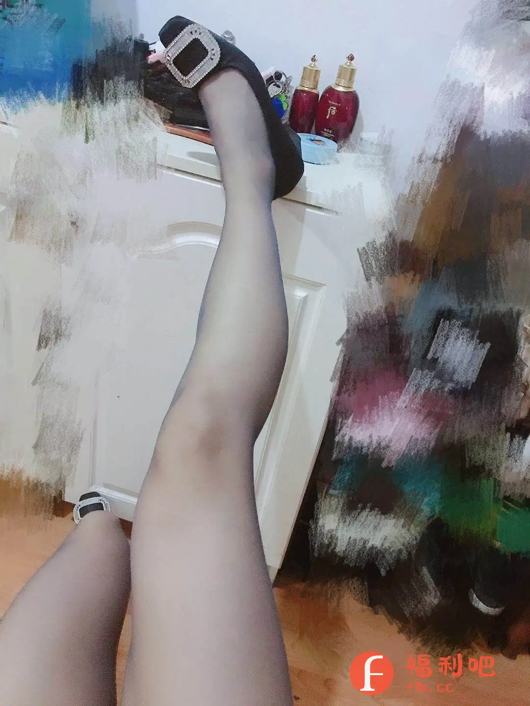 描述:一位女性展示了一双穿着黑色丝袜的美腿,一只脚穿着黑色方扣单鞋,鞋面装饰着闪亮的方扣,增添了时尚感。另一只脚则穿着另一只同款单鞋,姿势随意放松,展现出一种慵懒的魅力。背景是一个模糊的室内环境,有白色墙面和一些模糊的物品,可能是家居环境。整体画面给人一种精致、性感又略带随性的感觉,很适合作为时尚穿搭或者美腿展示的买家秀。