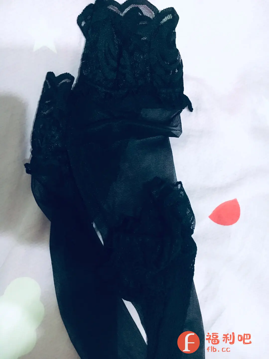 这是一张可能是某宝买家秀的照片,主体是一双黑色的丝袜,带有蕾丝花边设计,看起来比较性感。丝袜随意地摆放在一张白色的床上用品上,床单上还有一些星星的图案,以及一个红色的泪滴形状的图案。在画面的左下角,可以看到一个淡绿色的,形状类似云朵的装饰物。整体感觉比较随意,像是随手拍摄的。从丝袜的质感和花边设计来看,可能是一位年轻女性购买的,用来搭配服装的时尚单品。蕾丝花边的细节比较精致,可以看出丝袜的质量还不错。整张图片呈现出一种慵懒、随性的感觉,同时也带有一些性感和时尚的元素。:黑丝蕾丝袜