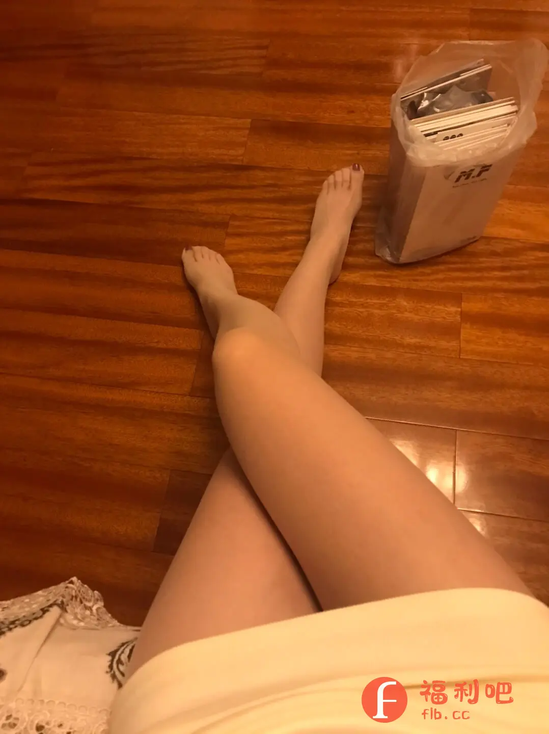描述:这张照片展示了一位女性舒适地坐在家中的地板上。她双腿交叉,穿着一件浅色的连衣裙或上衣,连衣裙边缘带有精致的蕾丝花边。地板是温暖的木质色调,营造出温馨的氛围。在她的脚边,有一个装满了书本或杂志的塑料袋,可能是刚从某宝购买的商品。她的脚趾甲涂着深红色的指甲油,增添了一丝精致感。整体画面给人一种轻松自在的感觉,也暗示了用户可能对网购的物品感到满意。照片的角度是从上往下拍摄的,更加突出了她的双腿和连衣裙。
