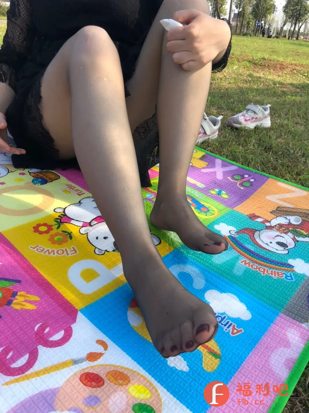 描述:图片展示了一位穿着黑色蕾丝连衣裙,搭配黑色丝袜的女士。她坐在色彩鲜艳的儿童爬行垫上,一手拿着白色纸巾,似乎在擦拭什么。她的脚上涂着深色指甲油,在阳光下显得格外醒目。背景是绿色的草地,以及两只儿童运动鞋,看起来像是带着孩子在户外玩耍。整个画面给人一种休闲放松的感觉,既展现了女性的优雅,又透露出妈妈的温柔。丝袜的质感和蕾丝的细节,也增加了画面的精致感。彩色地垫与黑色的服装形成了鲜明的对比,使得整体画面更具视觉冲击力。