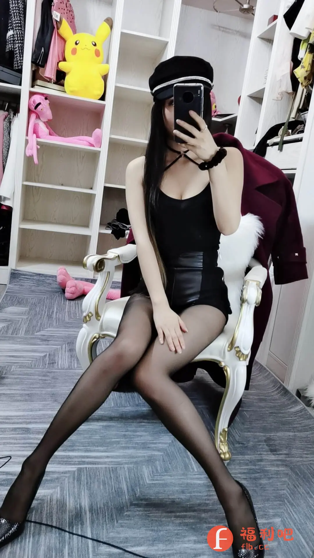 一位身材姣好的年轻女性坐在白色雕花椅上，优雅地展示着她的时尚穿搭。她头戴一顶潮流的黑色水手帽，一头柔顺的长发自然垂下，更显妩媚动人。上身穿着一件黑色吊带背心，搭配一条黑色皮质短裙，性感又时尚。腿上穿着黑色丝袜，脚踩一双亮片高跟鞋，更显腿部线条修长。她手持手机，正在自拍，展示她的完美身材和穿搭。背景是开放式衣帽间，里面摆满了各式各样的服装和玩偶，透露出精致的生活品味。整张照片的色调偏暗，更突显了她的时尚感和神秘感。这身装扮非常适合时尚派对或夜店，性感又不失个性。
