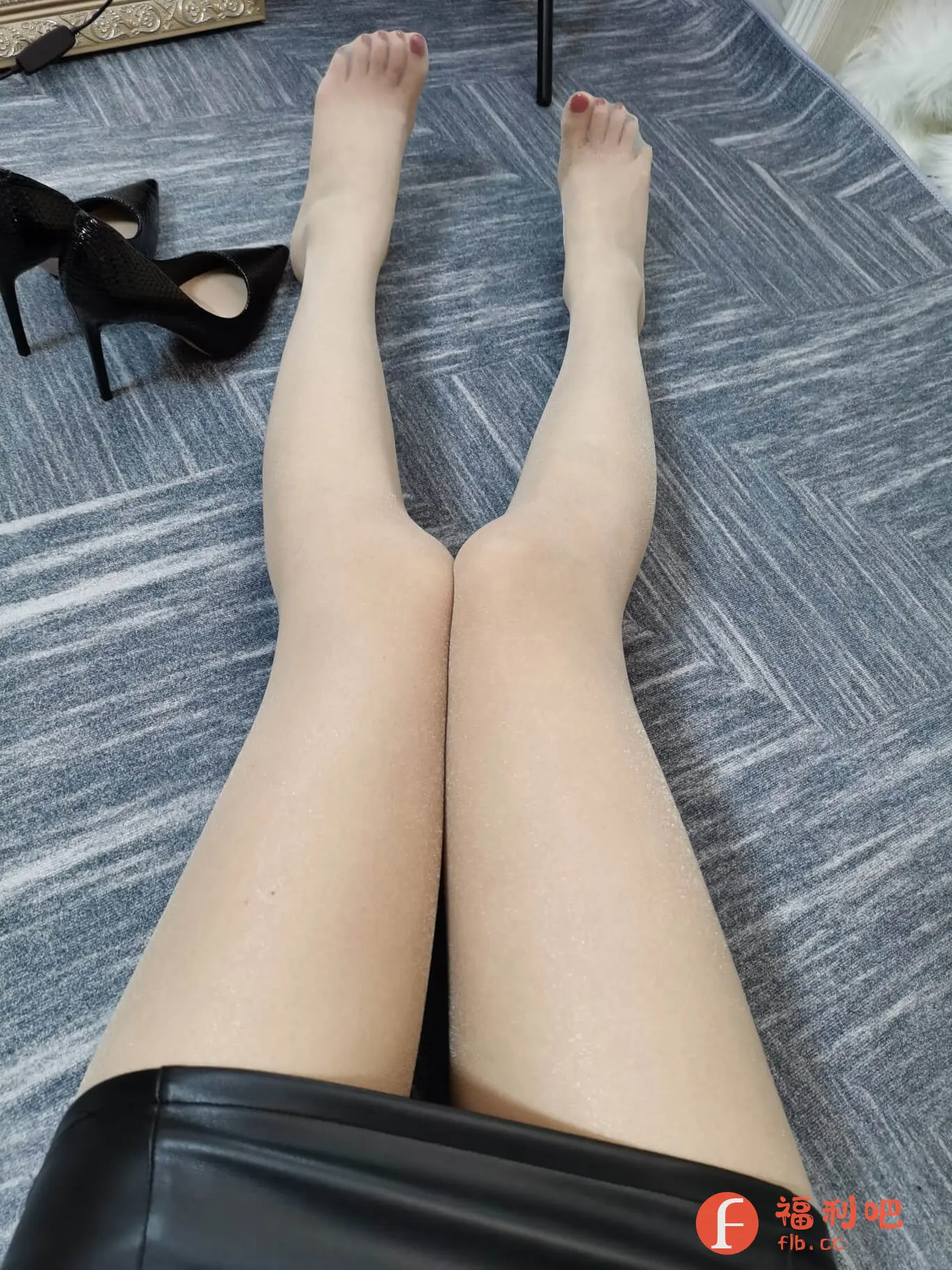 一位穿着黑色皮裙,搭配肉色丝袜的美女展示了一双修长的美腿。她赤裸着穿着丝袜的双脚随意地伸直放在地毯上,旁边放着一双黑色的高跟鞋。丝袜包裹着细腻的肌肤,腿型匀称笔直,给人以性感优雅的感觉。从拍摄角度来看,这是自上而下的俯拍视角,更加突出了腿部的线条,也展现了穿着皮裙带来的时尚感。整体画面简洁却不失美感,吸引人们的目光,可以推断这可能是一张服装或者丝袜的买家秀照片。