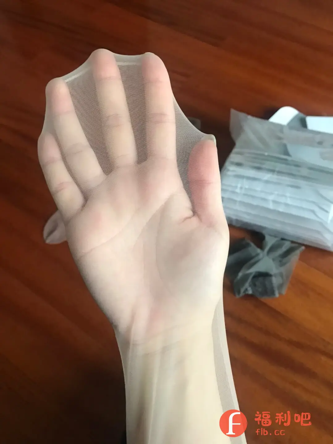 这张图片展示了一位美女在淘宝上购买的丝袜的买家秀。图片中,一只手撑开了一条浅色的丝袜,可以清晰地看到丝袜的材质非常轻薄透亮,几乎与肤色融为一体。手背的纹路和手指的形状透过丝袜都能清楚地辨认,可见其透明度之高。丝袜的颜色自然柔和,呈现出一种健康的光泽。背景是木质地板,旁边还有一些包装盒和塑料袋,可能是刚拆开的包裹。整体画面给人一种精致、时尚的感觉,突出了丝袜的质感和上身效果。这种买家秀照片对于其他潜在买家来说,能够提供更直观的参考,了解丝袜的真实颜色、透明度和舒适度。