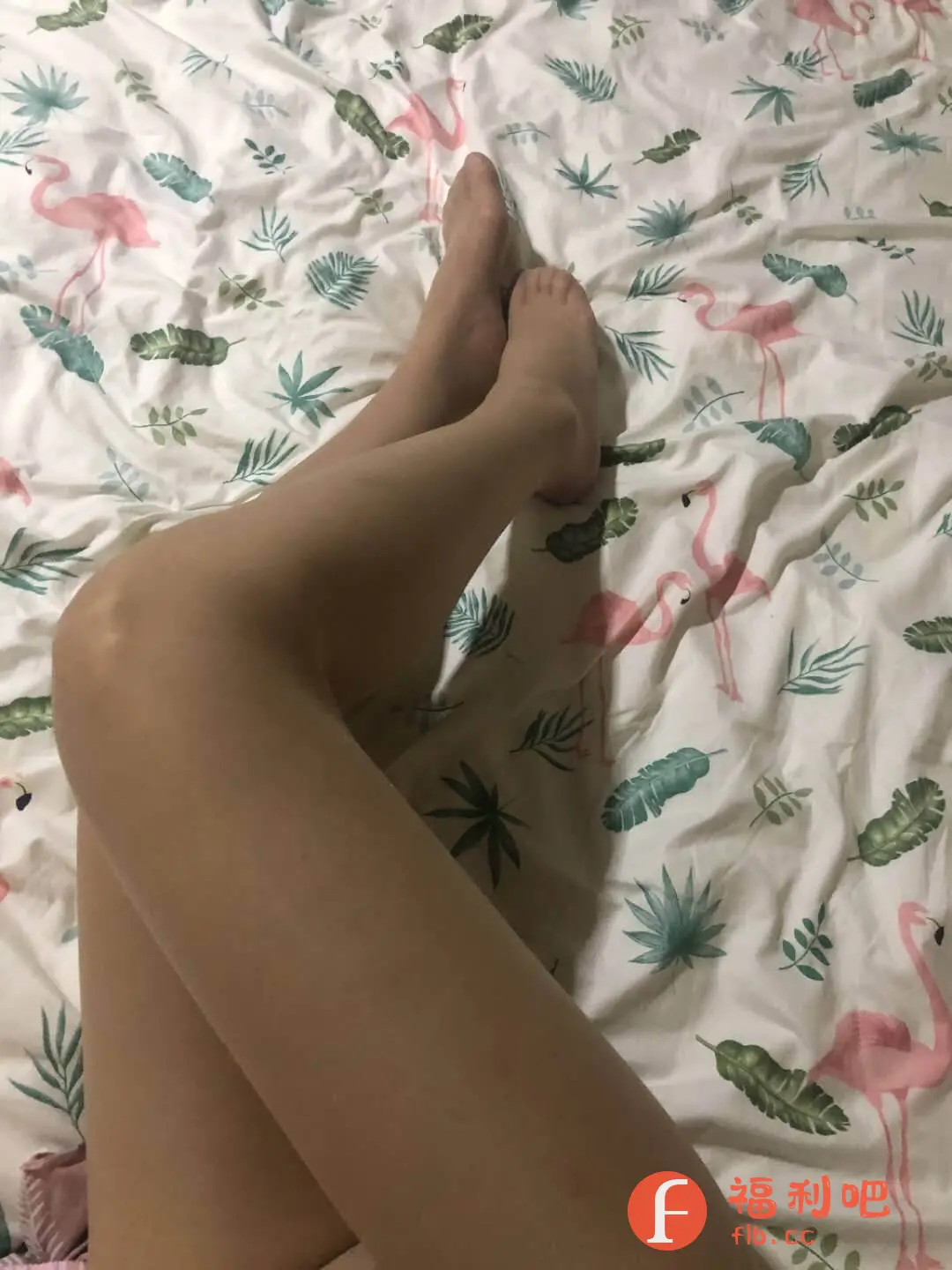 图中展示了一位穿着肉色丝袜的美女的双腿,她躺在铺着印有粉色火烈鸟和绿色植物图案的床上。双腿交叉,一只腿搭在另一只腿上,脚部也穿着同色系的丝袜。整体光线偏暗,营造出一种慵懒随意的氛围。背景的床单花纹鲜艳,与肉色丝袜形成对比,突出了腿部的线条。这可能是一张买家秀,旨在展示丝袜的颜色、质感以及穿着效果。从构图来看,重点突出了腿部,因此,用户可能是想展示自己购买的丝袜的上身效果。