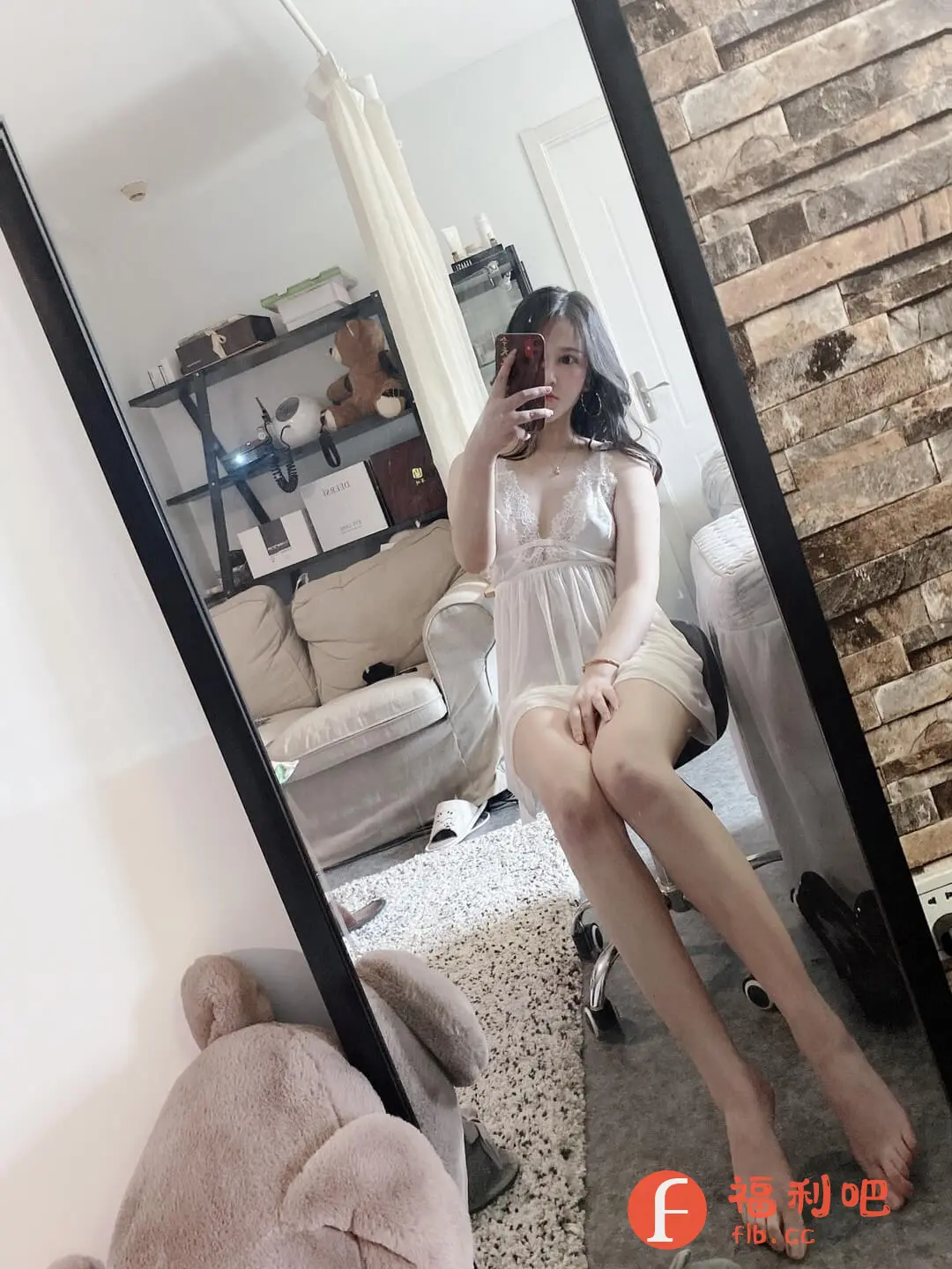 描述:这张照片是一位年轻女性穿着白色吊带睡裙在房间里自拍。她坐在一个灰色办公椅上,对着镜子举着手机,微微遮住了脸。睡裙的蕾丝边设计增添了几分性感,纤细的双腿自然地伸展着。房间的背景比较温馨,可以看到米色的沙发、置物架和毛绒玩具。镜子的边框是黑色的,反射出房间的整体布局。砖墙的纹理和地毯的颜色形成对比,营造出一种舒适的氛围。整体来看,这张照片展现了一种居家放松的状态,透露出一种随性而自然的美。