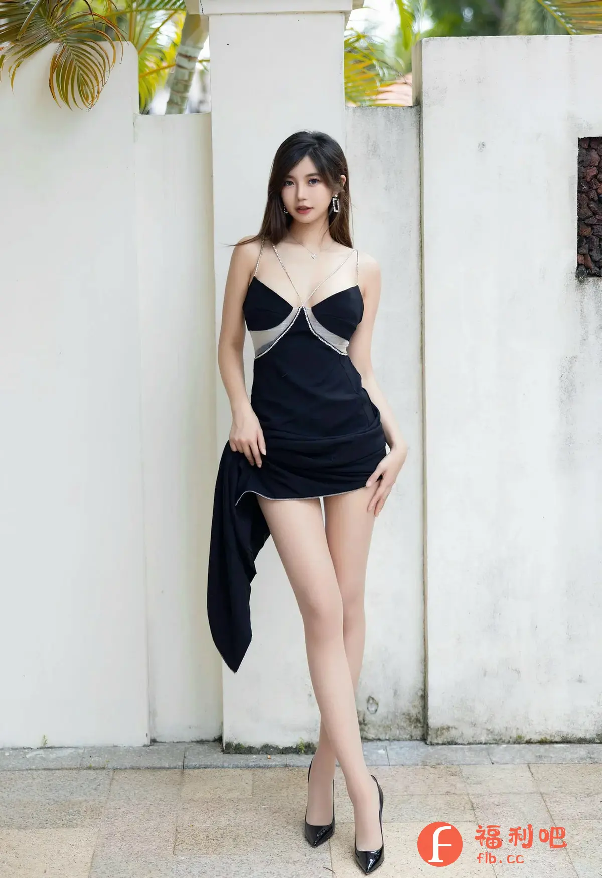 一位身材苗条的美女身穿一件黑色连衣裙,站在白色墙壁前拍摄了一张性感的写真照片。连衣裙的设计别致,带有银色亮片点缀的细肩带,胸前和裙边都镶有蕾丝,更显时尚。她微微提起裙摆,露出修长的双腿,搭配一双黑色高跟鞋,更显优雅气质。她的头发乌黑柔顺,佩戴着精致的耳环和项链,妆容精致,眼神迷人,散发出一种自信和妩媚的气息。背景是带有纹理的白色墙壁和一些绿色的植物,营造出一种简约而时尚的氛围。